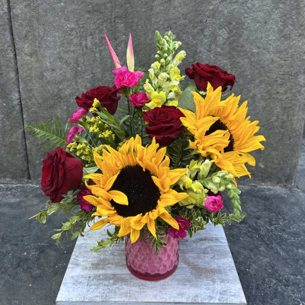 Bouquet of sunflowers, red roses, and pink flowers in a pink vase