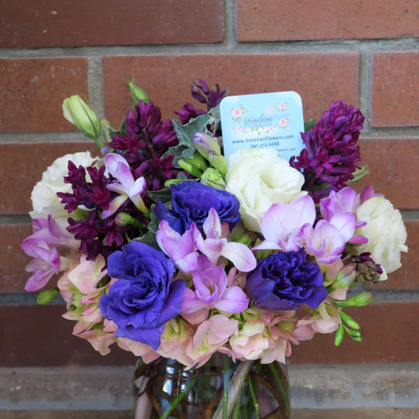 Round vase arrangement with purple, pink, and white flowers in a clear vase with branches inside