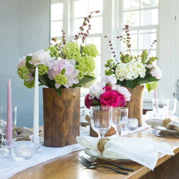 Floral table centerpieces with pink, white, and green blooms in wooden vases
