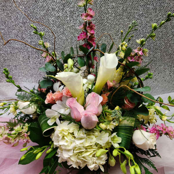 Low centerpiece of white calla lilies, hydrangeas, and pink roses with branches on a soft pink and silver backdrop