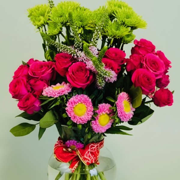 Pink roses and mixed daisies in a clear glass vase with a red ribbon