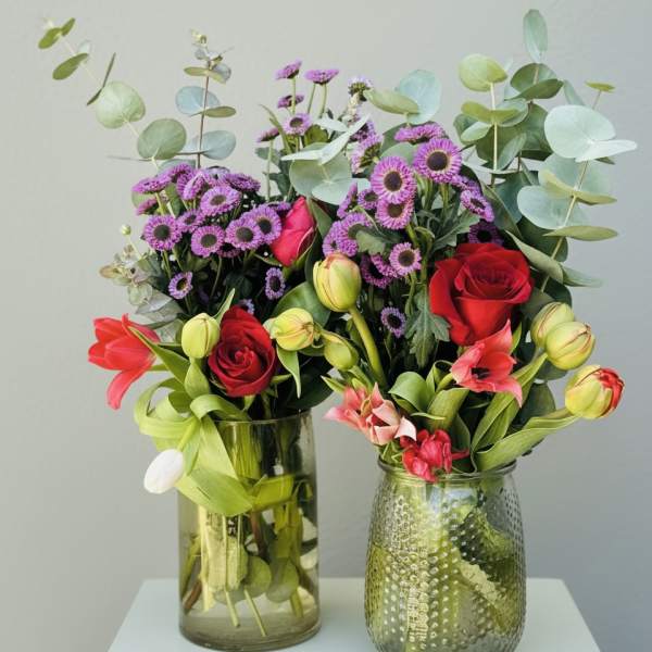 Two mixed flower arrangements in glass vases with red roses and purple blooms