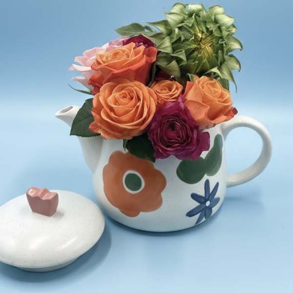 Orange and magenta roses arranged in a floral teapot with a matching lid.