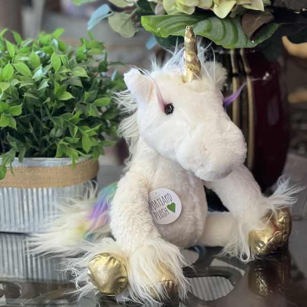 Plush unicorn with gold horn and hooves beside potted greenery and hydrangeas