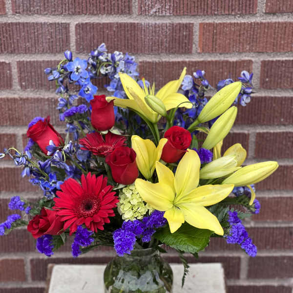 Bouquet of red roses, yellow lilies, and blue flowers in a glass vase