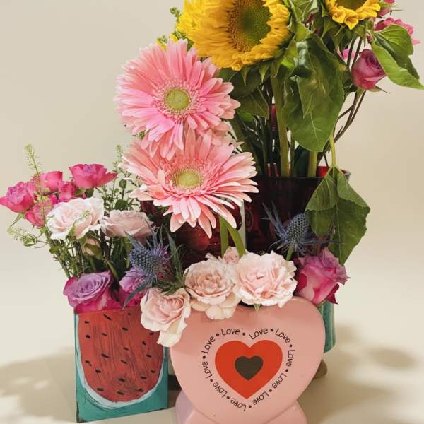 Mixed bouquet with sunflowers, pink gerberas, and roses in decorative containers