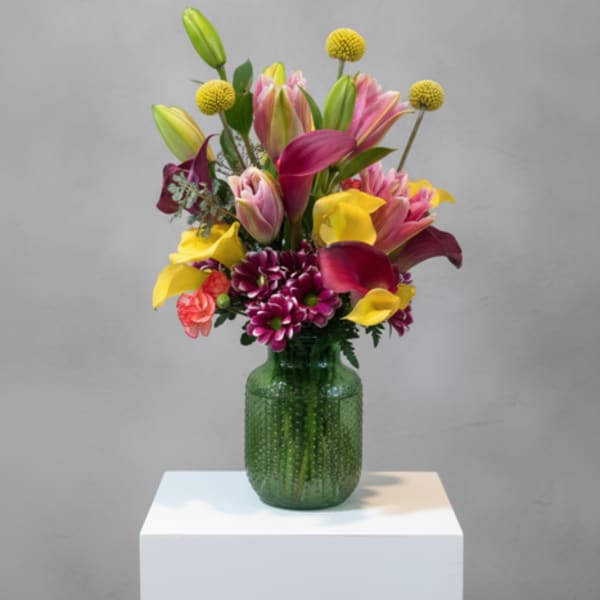 Colorful bouquet of lilies, calla lilies, and mums in a green glass vase