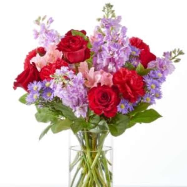 Bouquet of red roses and purple flowers in a clear glass vase