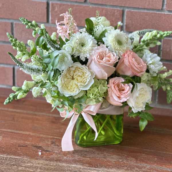 Compact arrangement of blush roses and white blooms in a green glass cube vase with pink ribbon