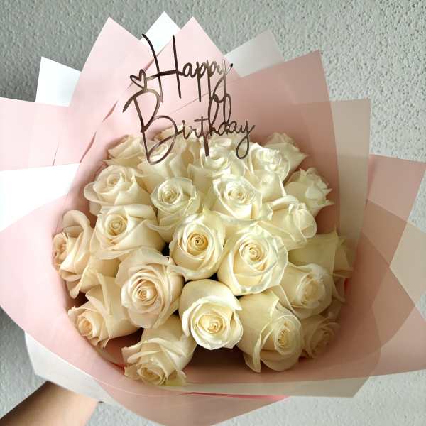 Bouquet of cream roses wrapped in pink paper with a Happy Birthday topper