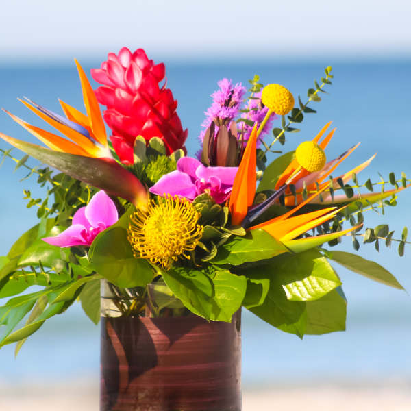 Tropical bouquet with bird of paradise, pink blooms, and yellow pincushion flowers in a vase