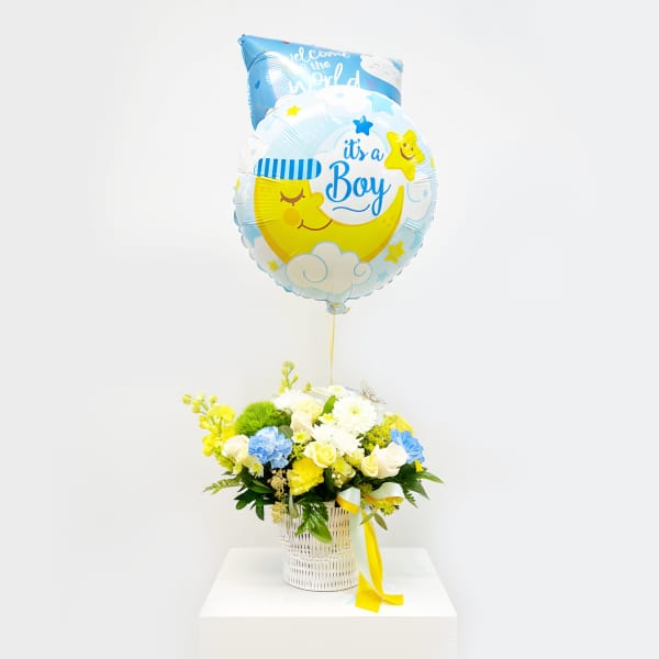 Blue baby boy balloon above a white basket of yellow and white flowers