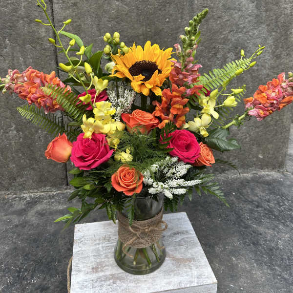 Bright mixed bouquet with sunflowers, roses, and orchids in a glass vase