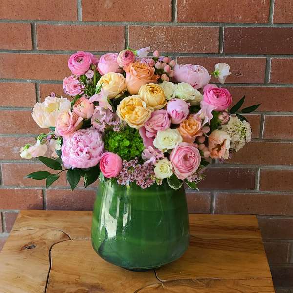 Mixed pastel flower arrangement in a green glass vase