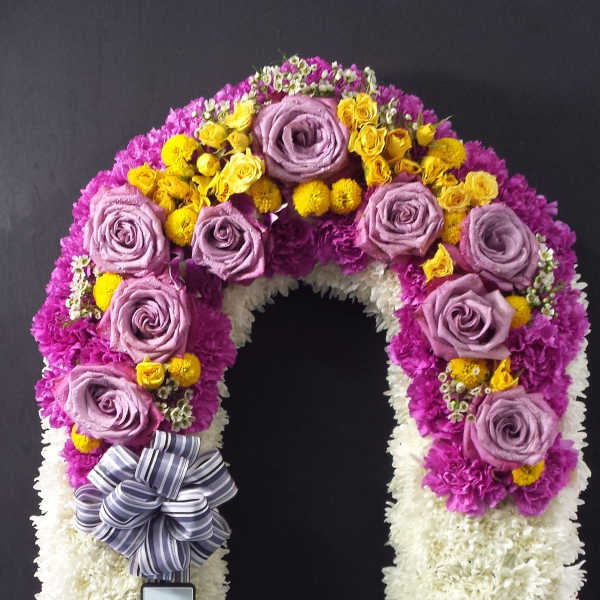 U-shaped floral wreath with purple, white, and yellow blooms and a striped ribbon bow