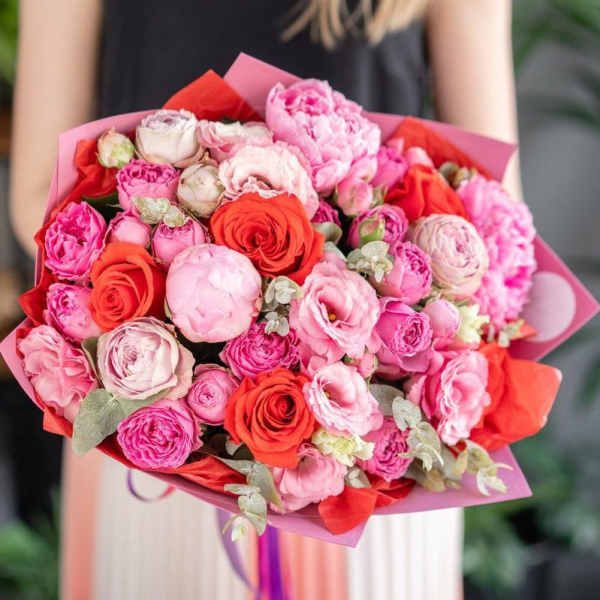 Handheld bouquet of pink and red roses wrapped in pink paper