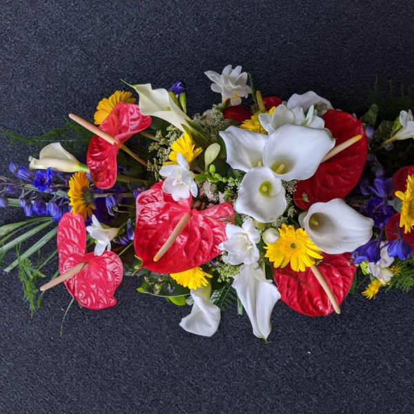 Long floral arrangement with red anthuriums, white calla lilies, and yellow daisies