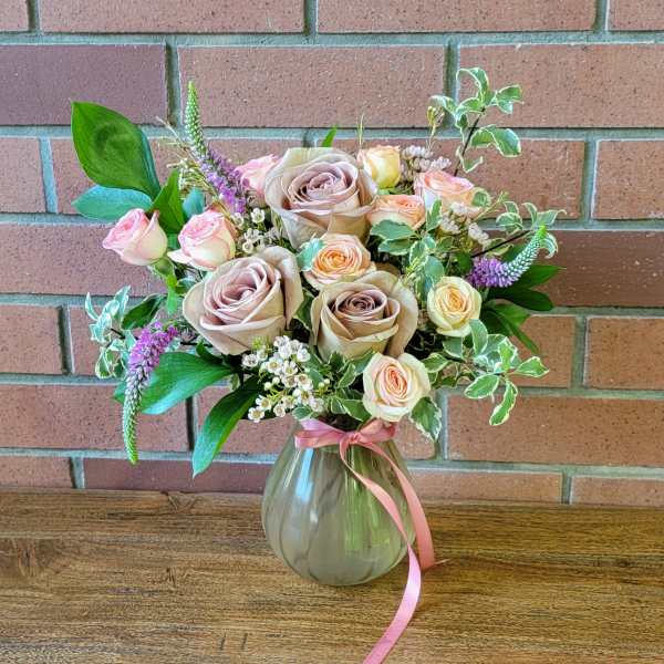 Bouquet of blush and peach roses in a glass vase with a pink ribbon