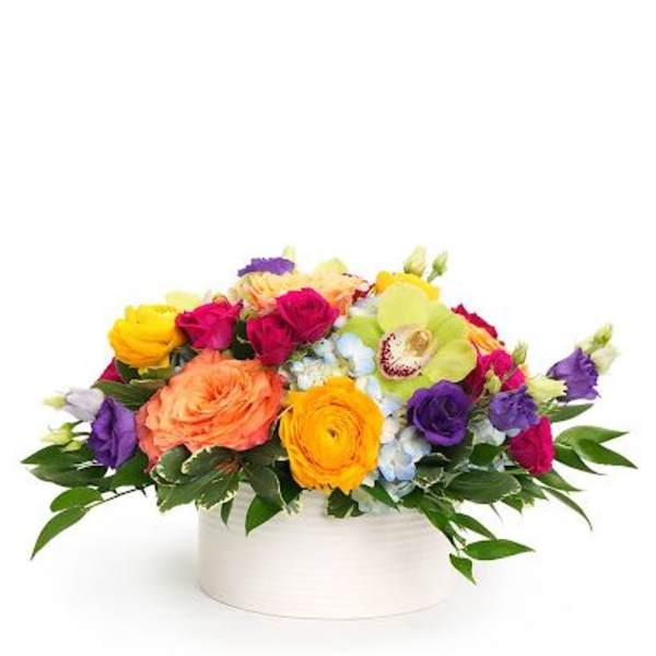 Low arrangement of bright mixed flowers in a white round vase