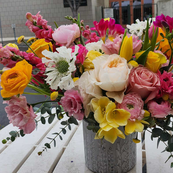 Colorful arrangement of pink roses, yellow blooms, and mixed flowers in a gray textured vase