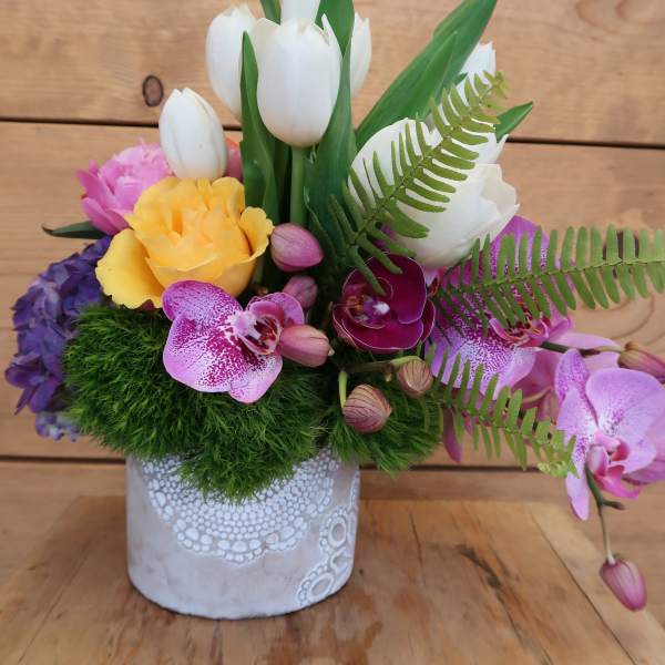 Colorful floral arrangement in a white decorative pot with tulips and orchids
