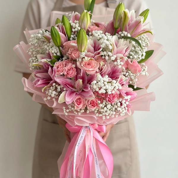 Pink lilies and roses bouquet wrapped in pink paper with a ribbon
