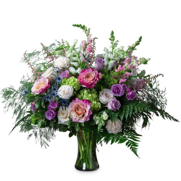 Large mixed bouquet of pink, purple, and white flowers with green hydrangeas in a clear glass vase