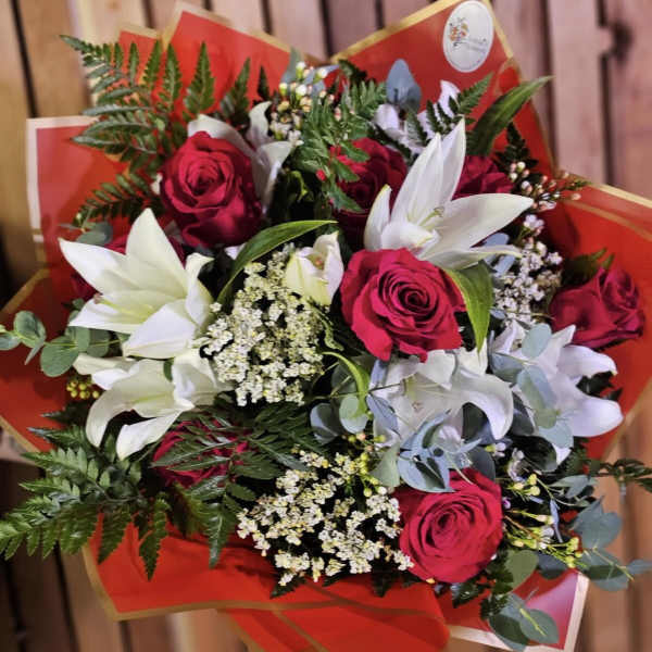 Bouquet of red roses and white lilies with mixed greenery in red wrap