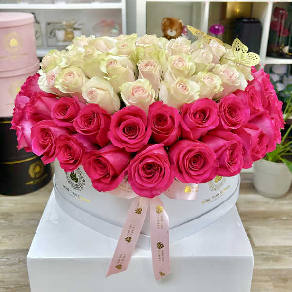 Round hatbox of pale ivory and bright pink roses with a ribbon and gold butterfly accents