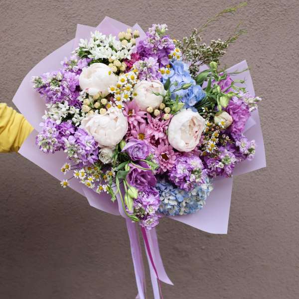 Pastel bouquet with pink, purple, blue, and white flowers wrapped in lavender paper