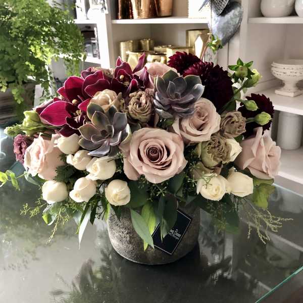 Mixed bouquet with pale roses, dark orchids, and succulents in a stone vase