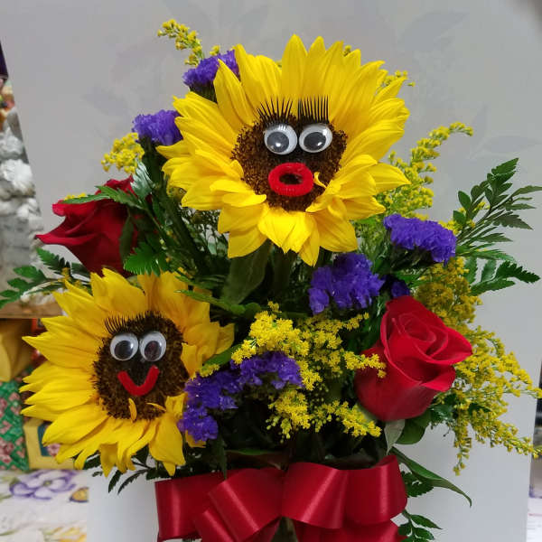 Bouquet with sunflowers, red roses, and a red ribbon in a glass vase