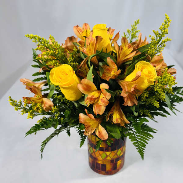 Yellow roses and orange alstroemeria in a mosaic glass vase.