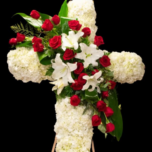 Cross-shaped floral tribute with red roses, white lilies, and white hydrangeas