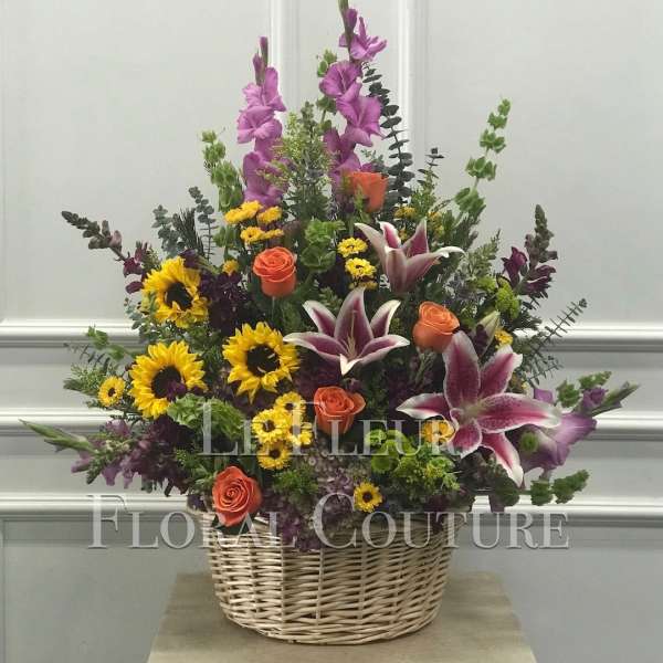 Basket arrangement with sunflowers, roses, lilies, and purple spikes