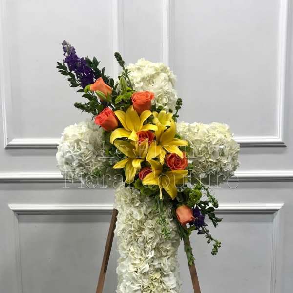 Cross-shaped floral arrangement with white hydrangeas, yellow lilies, and orange roses