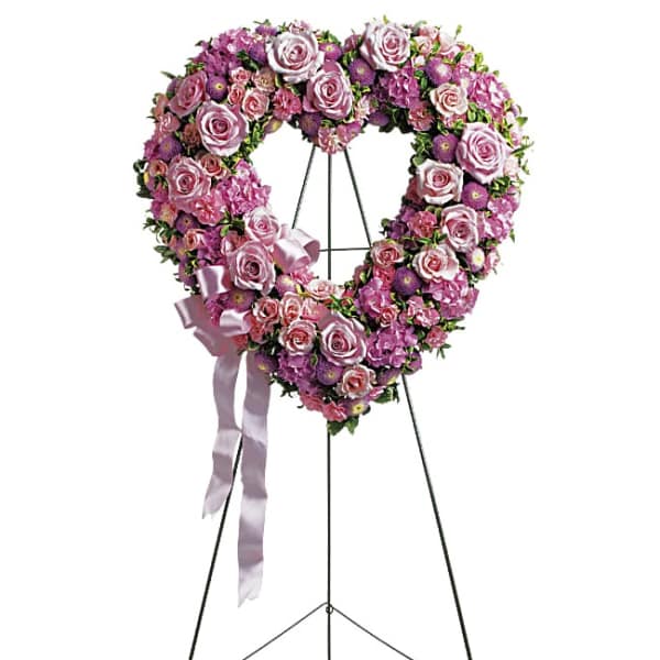 Heart-shaped pink and purple floral wreath on a stand with a ribbon