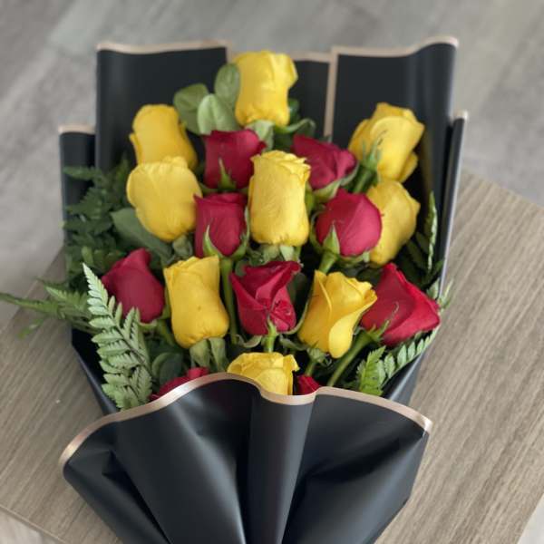 Bouquet of red and yellow roses wrapped in black paper with a red bow