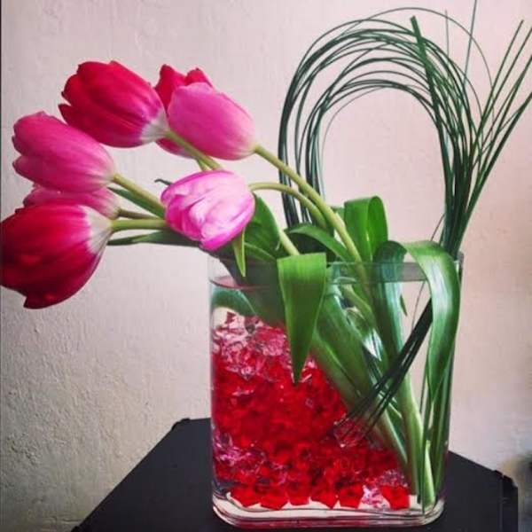 Pink and red tulips in a clear glass vase with red decorative stones