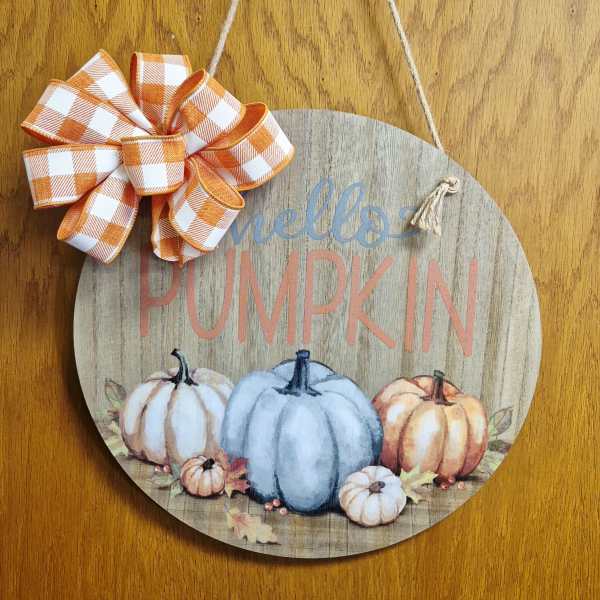 Round wooden pumpkin sign with orange plaid bow hanging by twine
