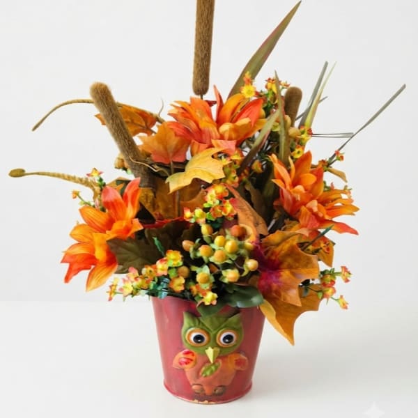 Autumn floral arrangement in a red owl pot with orange flowers and cattails