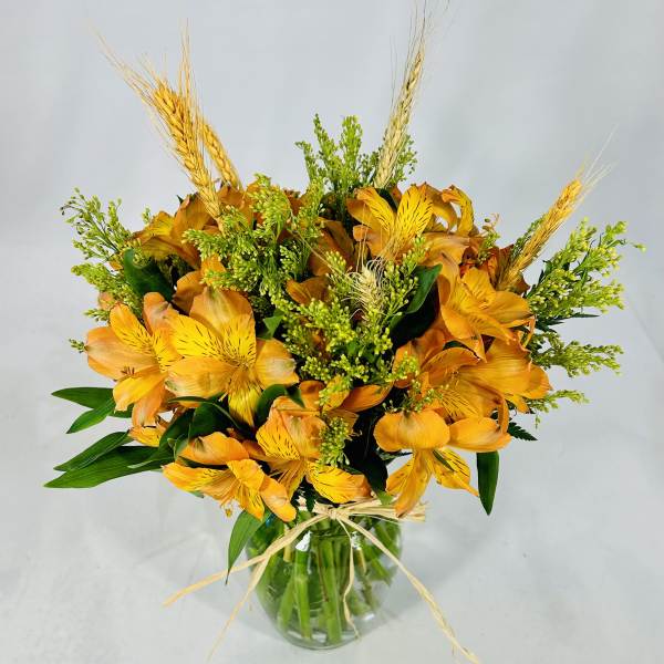 Orange alstroemeria bouquet in a clear glass vase with wheat accents