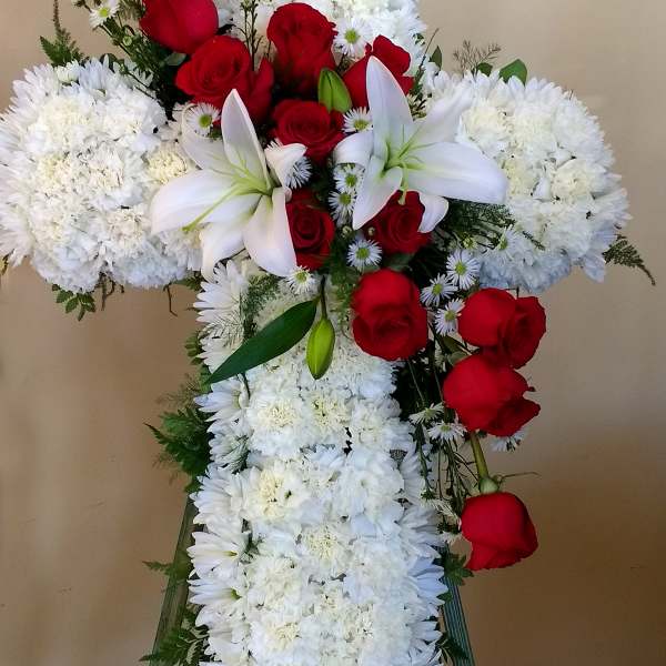 Cross-shaped floral tribute with red roses, white lilies, and white chrysanthemums