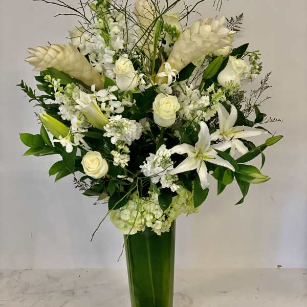 White floral arrangement in a tall green vase with lilies and roses
