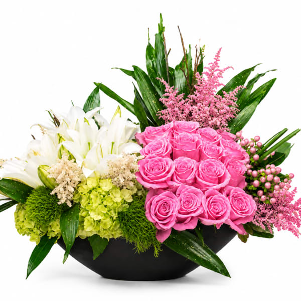 Pink roses and white lilies in a black bowl vase with green hydrangeas