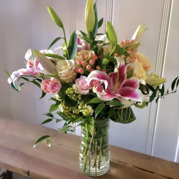 Mixed bouquet of pink lilies, roses, and spray roses in a clear glass vase