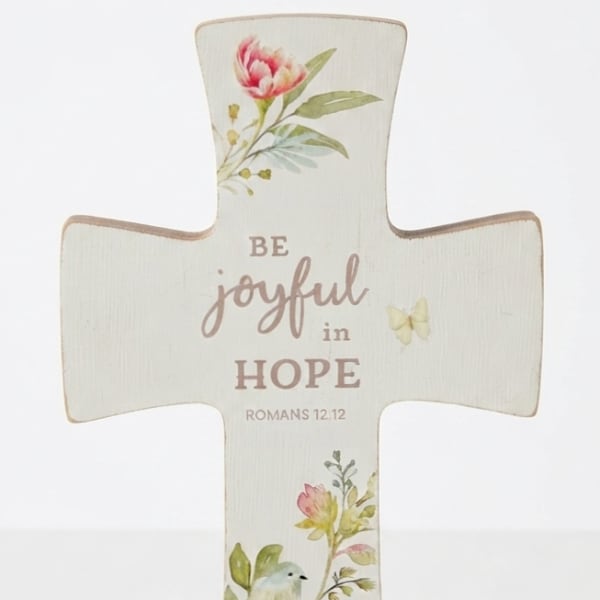 Cross-shaped decorative sign with floral print and the words "Be joyful in hope"