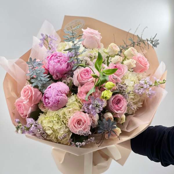 Hand-tied bouquet of pink roses, peonies, and hydrangeas in blush wrap