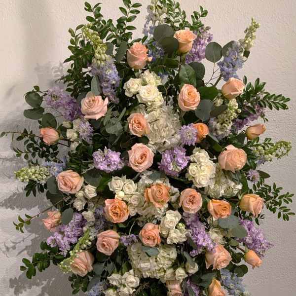 Large floral spray of peach roses, white blooms, and lavender flowers on an easel