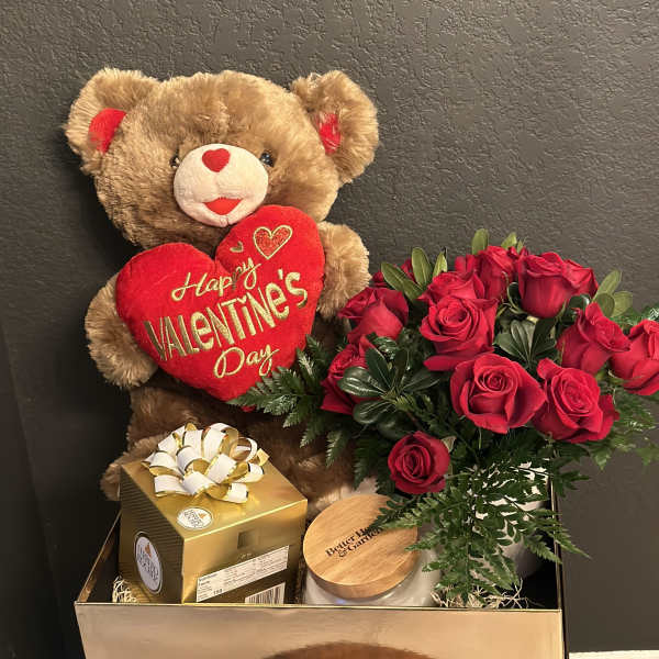 Teddy bear with a Valentine heart beside red roses and gift boxes